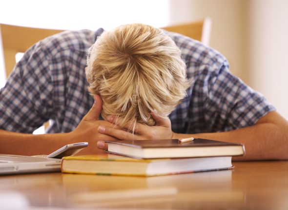 A boy lies his head down on the table while doing homework