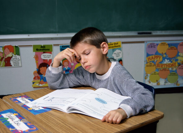 A young Caucasian boy sitting at a desk in a classroom doing homework